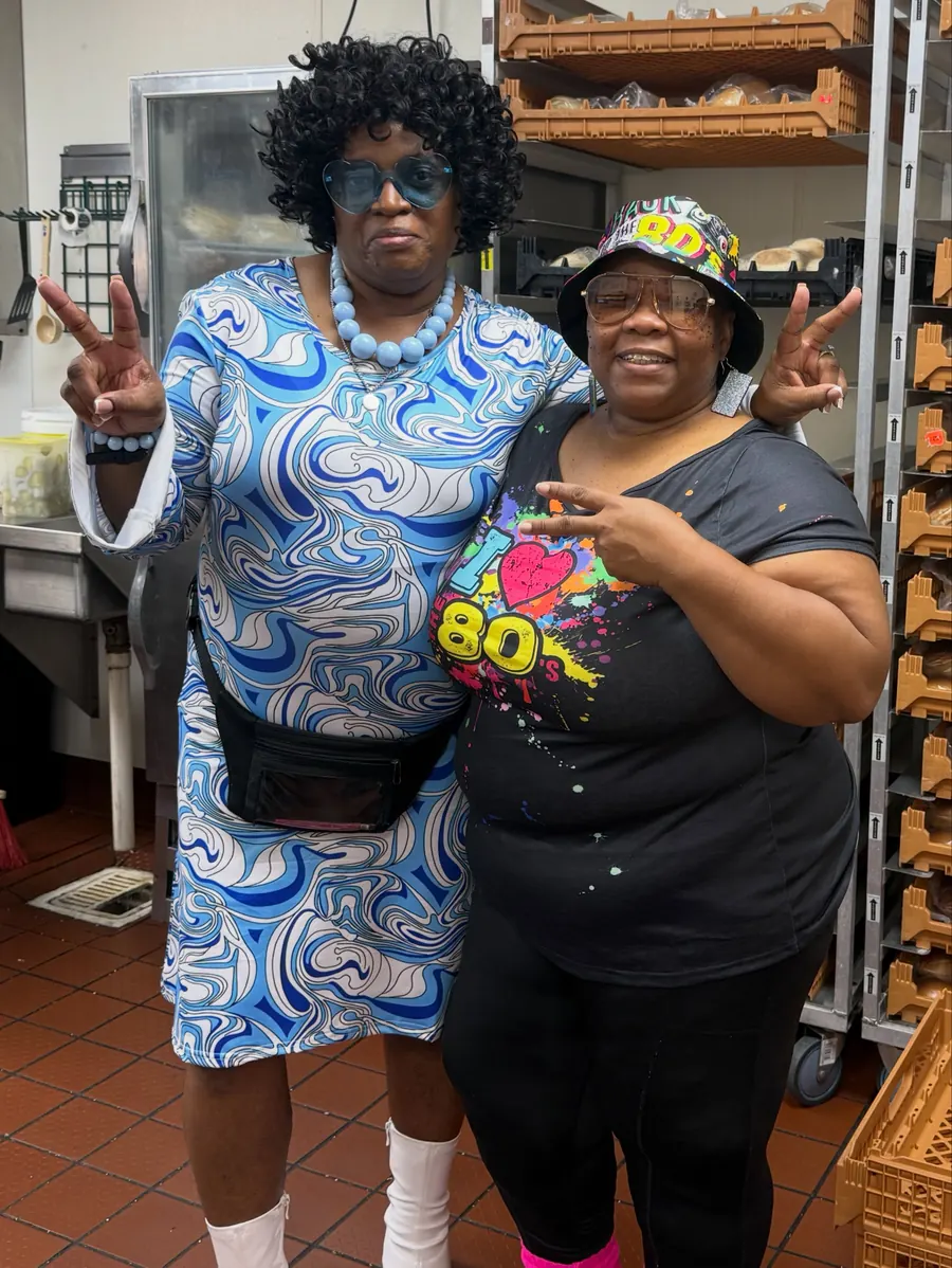 Crew member in a curly wig and tie-dye with a teammate for Throwback Thursday
